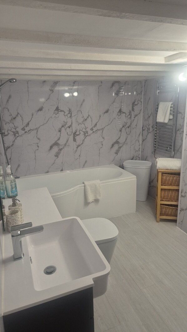 A modern bathroom with a marble wall, a bathtub, a sink, and a small wicker basket.