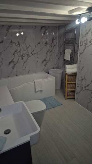 A bathroom with a bathtub, toilet, sink, and a mirror with lights. - Cool, Calm Georgian Apartment base in Shrewsbury -pet friendly (Shrewsbury)
