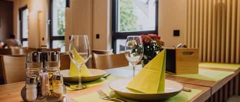 Una mesa de comedor con platos, vasos y un porta servilletas, con vista a una ventana al fondo.