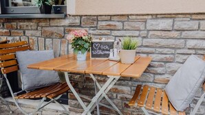 An outdoor seating area with a wooden table and chairs, a sign with 'Willkommen' (welcome), and potted plants. - Pascals Ruhestube (Mörsdorf)
