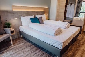 A modern hotel room with a bed, bedside table, lamp, and a small plant.