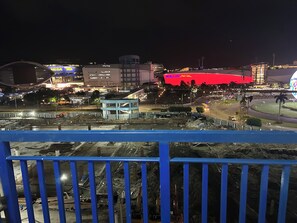 Ein nächtliches Stadtbild mit einem markanten, rot beleuchteten Gebäude, einer blau beleuchteten Struktur und einer belebten Kreuzung.