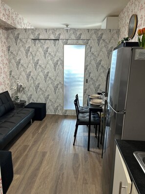 Ein gemütlicher Wohnraum mit Sofa, Esstisch, Stühlen, einem Kühlschrank und einem Fenster mit Aussicht.