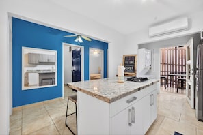 A modern kitchen with a central island, white cabinets, a blue accent wall, and a dining area with a table and chairs. - Comfort By The Sea (Roatan)