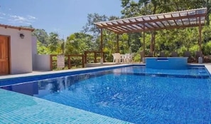 Una piscina con pérgola, un pequeño edificio y mobiliario de exterior.