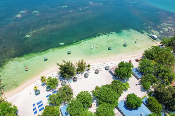 An aerial view of a beach resort with clear waters, a jet bridge, and a boat dock. - Comfort By The Sea (Roatan)