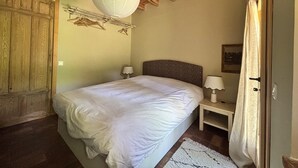 A bedroom with a wooden ceiling, a bed with white bedding, a nightstand with a lamp, and a door with a curtain. - House by the River in Santa María de la Alameda (El Pimpollar)