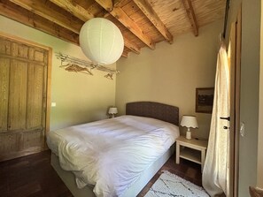 Ein Schlafzimmer mit Holzboden, einem Bett mit weißer Bettwäsche, einem Nachttisch mit Lampe und einer Tür mit Vorhang.