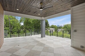 Ein offener Balkon mit Schachbrettmuster-Boden, einem Deckenventilator und Blick auf Bäume und Gebäude.