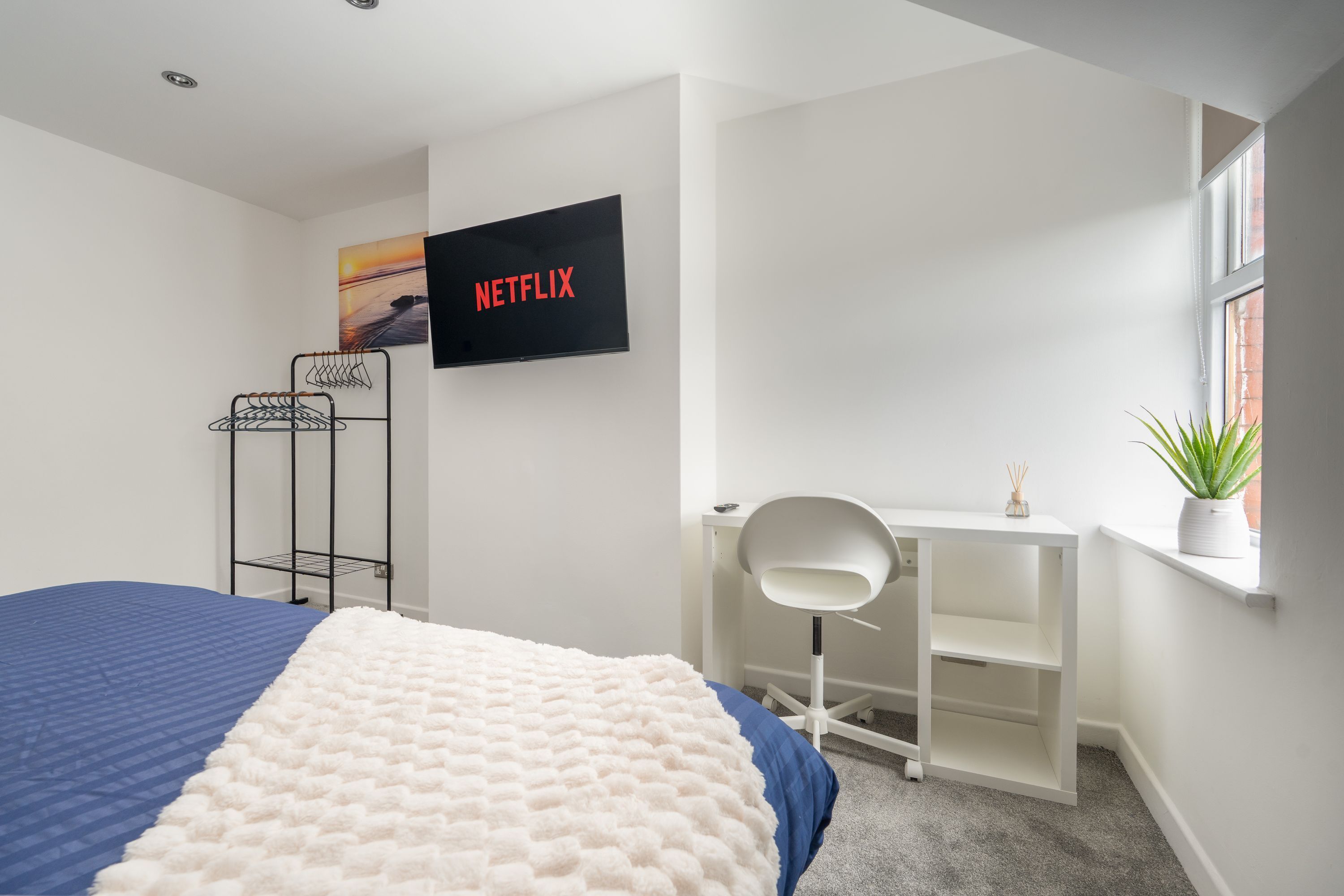 Un dormitorio con cama, escritorio, silla, televisor y ventana.