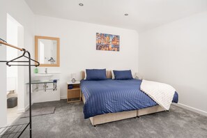 Quarto com cama, mesa de cabeceira, espelho, cabideiro e um quadro na parede.