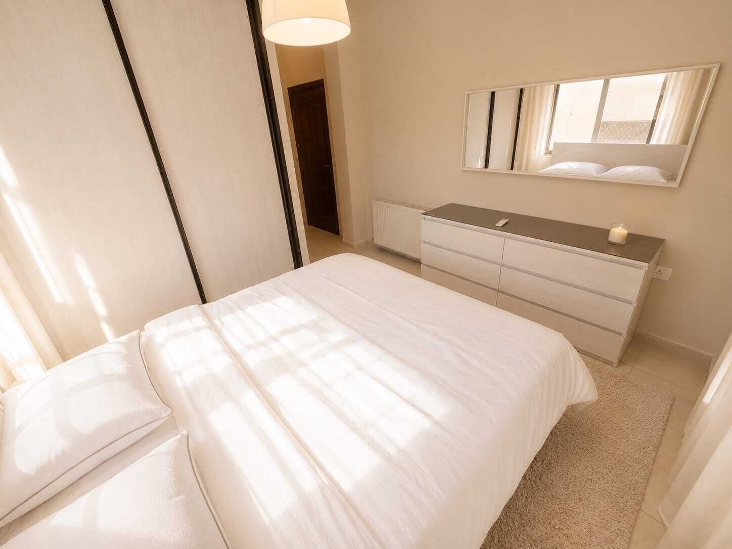 Une chambre à coucher avec un lit, une commode, un miroir et une porte.