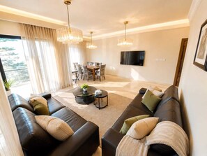 Ein modernes Wohnzimmer mit einer Eckcouch, einem Couchtisch, einem Essbereich mit Stühlen und einem flachbildfernseher an der Wand.
