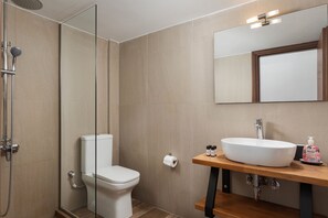 Ein Badezimmer mit einer gläsernen Duschkabine, einer weißen Toilette, einem Holzwaschtisch mit einem großen weißen Waschbecken und einem Spiegel über dem Waschbecken.