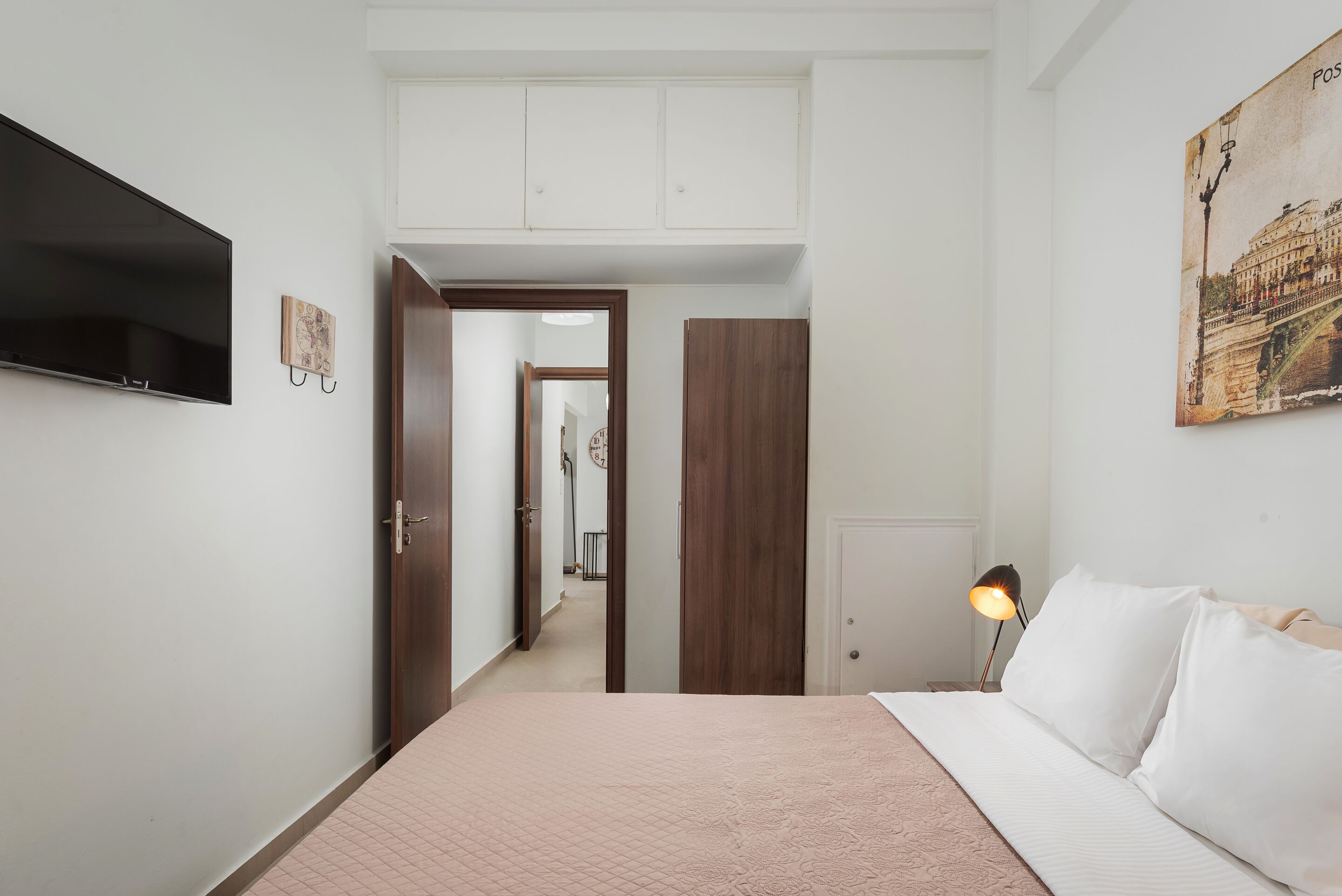 A bedroom with a bed, a TV, a lamp, and a door leading to a hallway.