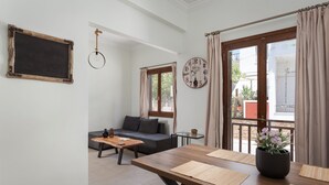 Una sala de estar con un sofá, una mesa de centro y una mesa de comedor de madera. Hay un reloj en la pared y una ventana con cortinas.