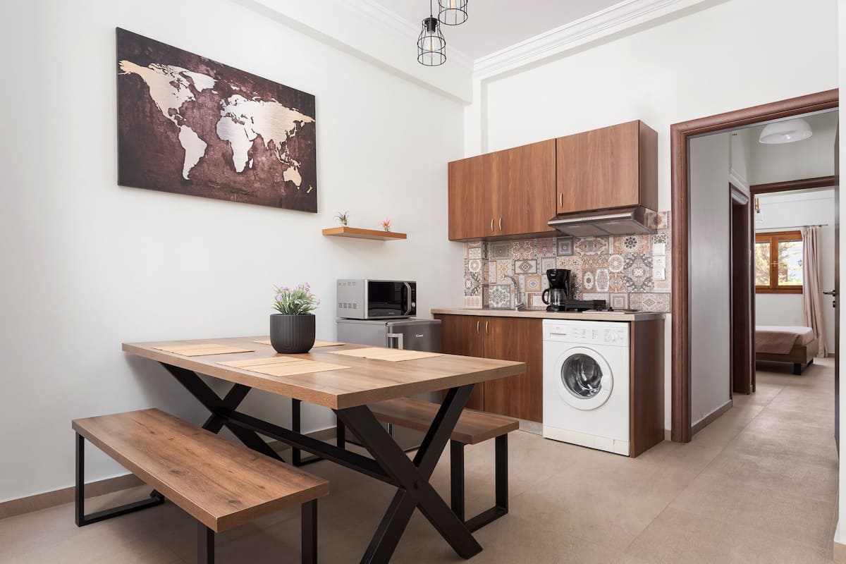 Uma cozinha compacta com armários de madeira, micro-ondas, máquina de lavar e uma mesa de jantar com bancos.