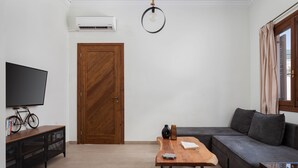 Una sala moderna con puerta de madera, televisor sobre un mueble, sofá, mesa con un jarrón y lámpara colgante.