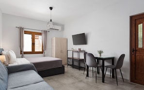 A modern bedroom with a bed, a desk with chairs, a TV, and a wardrobe. - Utopia Suites (Egina)