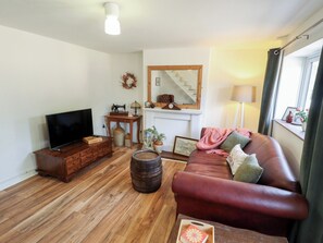 A living room with a TV, wooden furniture, a sofa, a fireplace, and a window with curtains. - The Monks Retreat (King's Lynn)