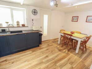 A kitchen with a central island, a dining table with chairs, and a clock on the wall. - The Monks Retreat (King's Lynn)