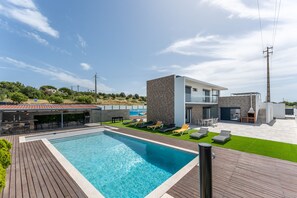 Ein modernes Haus mit Swimmingpool, Gartenmöbeln und einer Terrassenfläche.