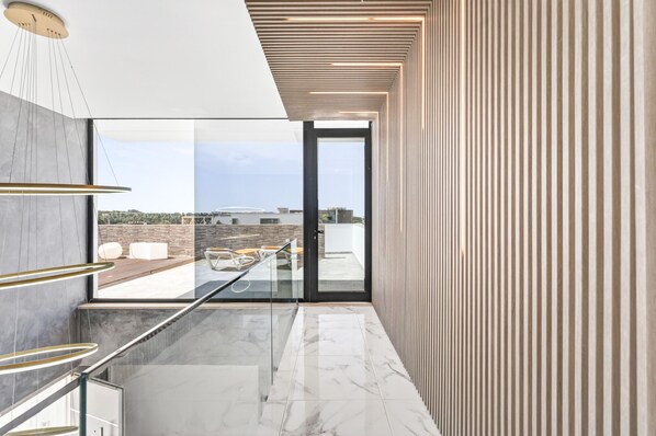 Ein modernes Interieur mit einer Glastür, die auf eine Terrass im Freien führt, einem Marmorboden und einer Holzdielendecke.