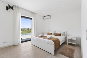 Ein modernes Schlafzimmer mit Bett, Nachttischen, einer Klimaanlage und Blick durch ein großes Fenster.