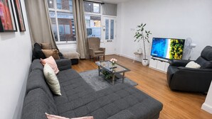 Una sala de estar moderna con un sofá gris, una mesa de centro de vidrio, un televisor de pantalla plana y una planta.