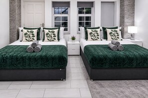 A twin bedroom with two beds, each with a green leaf-patterned bedspread, white pillows with green leaf designs, and a small bedside table with a lamp. - Modern 2-Bedroom flat in Marylebone near Paddington & Edgware Road with Wi-Fi (London)