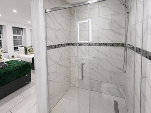 A modern bathroom with a glass-enclosed shower, white marble tiles, and a green bedspread. - Modern 2-Bedroom flat in Marylebone near Paddington & Edgware Road with Wi-Fi (London)