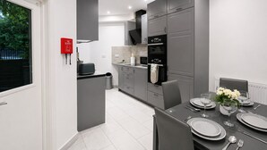 Cocina moderna con armarios grises, horno negro y comedor con platos y cubiertos.