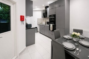 A modern kitchen with grey cabinets, a black oven, and a dining area set with plates and cutlery. - Modern 2-Bedroom flat in Marylebone near Paddington & Edgware Road with Wi-Fi (London)