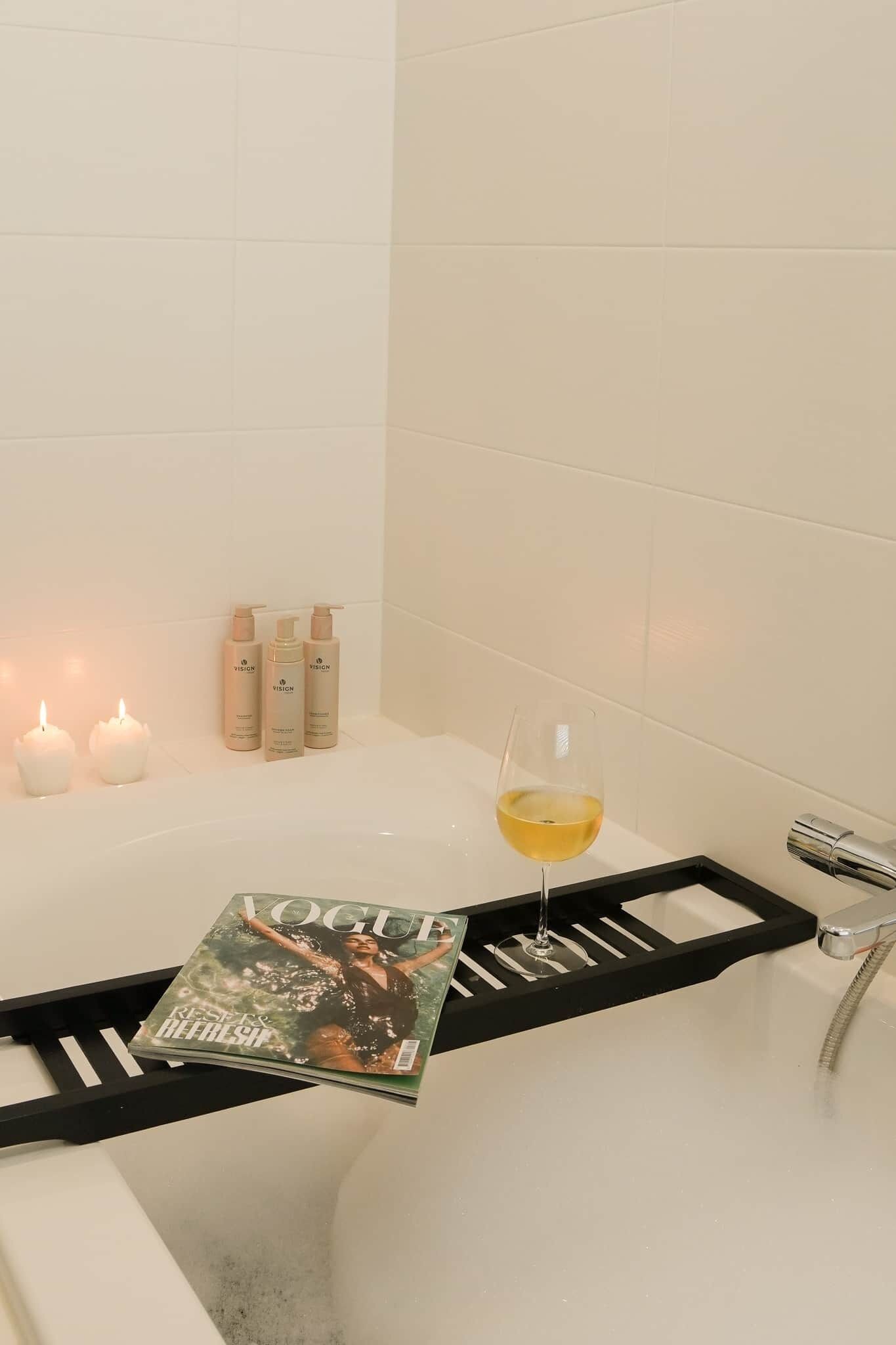 Un baño con bañera, velas, artículos de aseo y una revista.