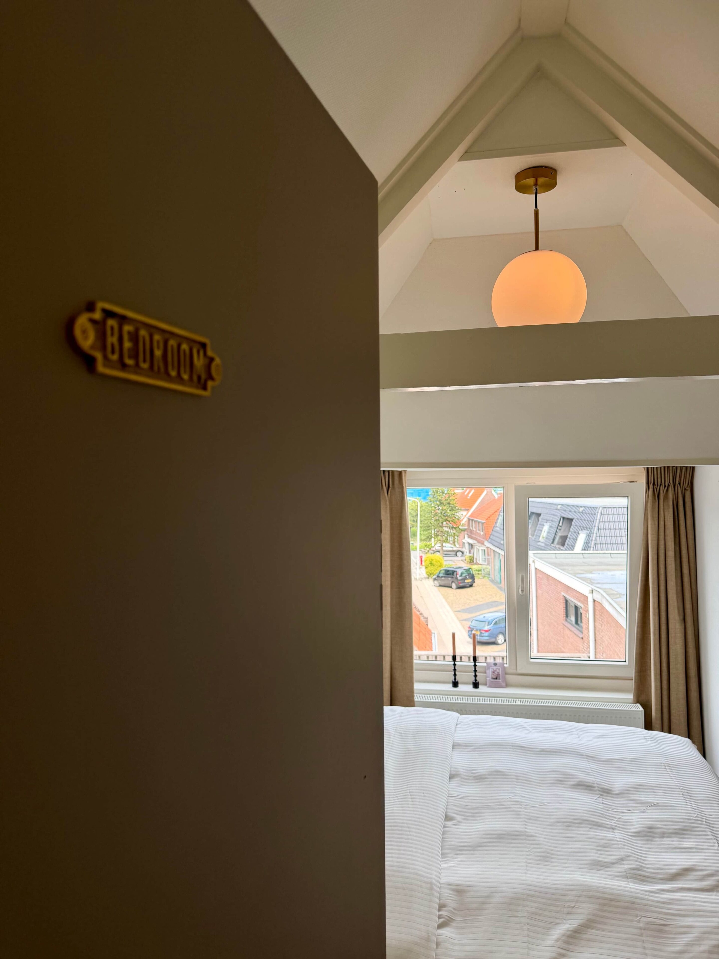 Een slaapkamer met een bed, een plafondlamp, een raam met gordijnen en een bord aan de muur.