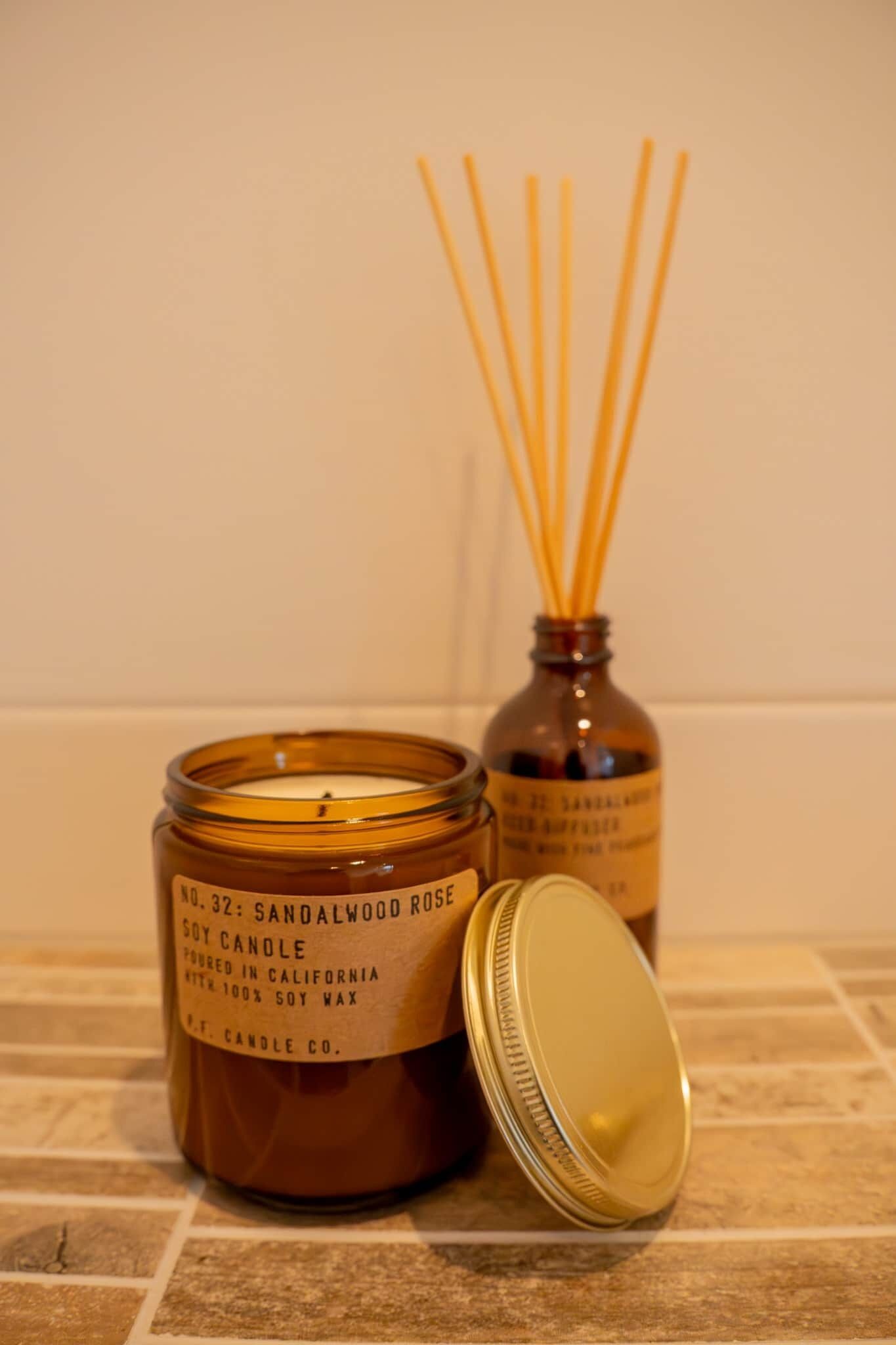 A candle with a label, a candle jar, and a bottle with reed sticks.
