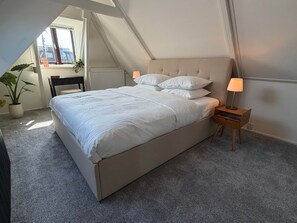 Une chambre à coucher avec un lit, des lampes de chevet, une chaise, une plante en pot et une vue par la fenêtre.