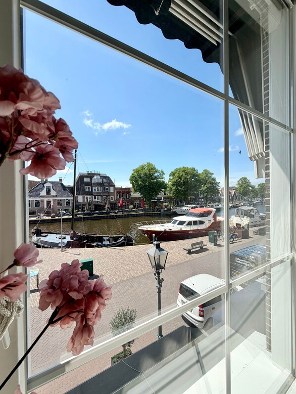 A window view of a canal with boats, a white car, and a building with red awnings.