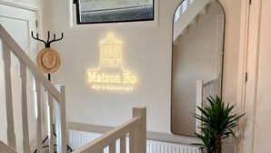 A modern interior with a staircase, a neon sign reading 'Maison Bo BED & BREAKFAST,' a television mounted above a window, and a large mirror. - Maison Bo | Luxury Stay in Historic Lemmer (Lemmer)