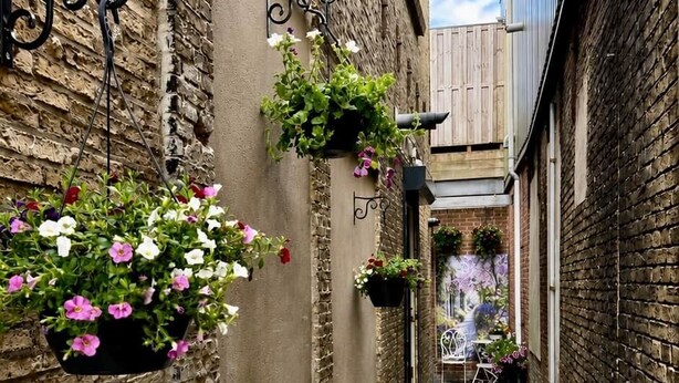 A narrow alleyway with hanging flower baskets and a tiled floor. - Maison Bo | Luxury Stay in Historic Lemmer (Lemmer)