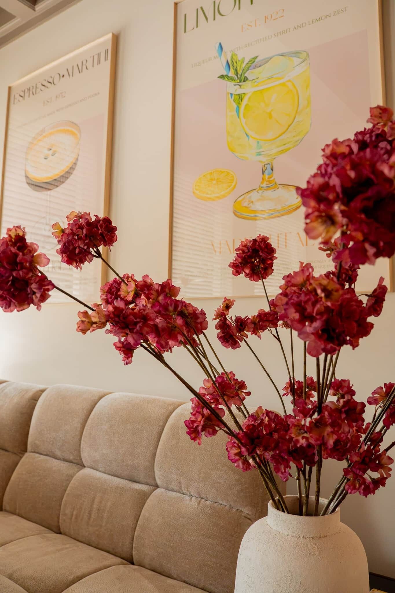 A beige sofa and a vase with pink flowers against a wall with framed artwork.