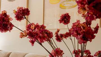 A beige sofa and a vase with pink flowers against a wall with framed artwork.
