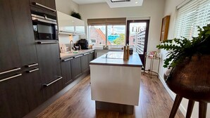 A modern kitchen with dark cabinetry, a central island, and a view of the city through large windows. - Maison Bo | Luxury Stay in Historic Lemmer (Lemmer)