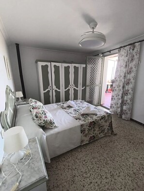A hotel room with a bed, a desk with a lamp, a ceiling fan, and a view of the outside.