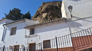 A building with white walls, a balcony with a metal railing, and a rocky cliff in the background.