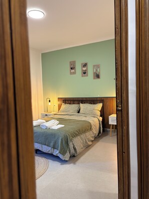 Ein Schlafzimmer mit Bett, Nachttisch, Wandbild und einer Tür.