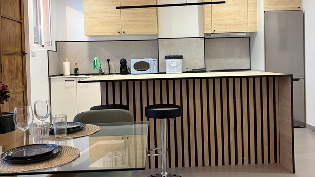 A modern kitchen with wooden cabinets, a stainless steel refrigerator, and a bar area with stools. - 3 Bedrooms by Ruzafa, metro 1 min, A/C (València)