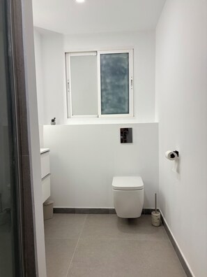 Une petite salle de bain propre, avec des toilettes, une fenêtre et une petite étagère.