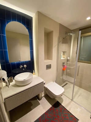 Un baño moderno con un espejo grande, un lavabo, un inodoro y una ducha con mampara de vidrio.