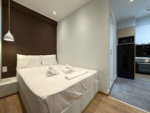 A modern hotel room with a neatly made bed, a built-in oven, and a separate kitchen area. - SmartLiving Central Apt 3 (Thessaloniki)